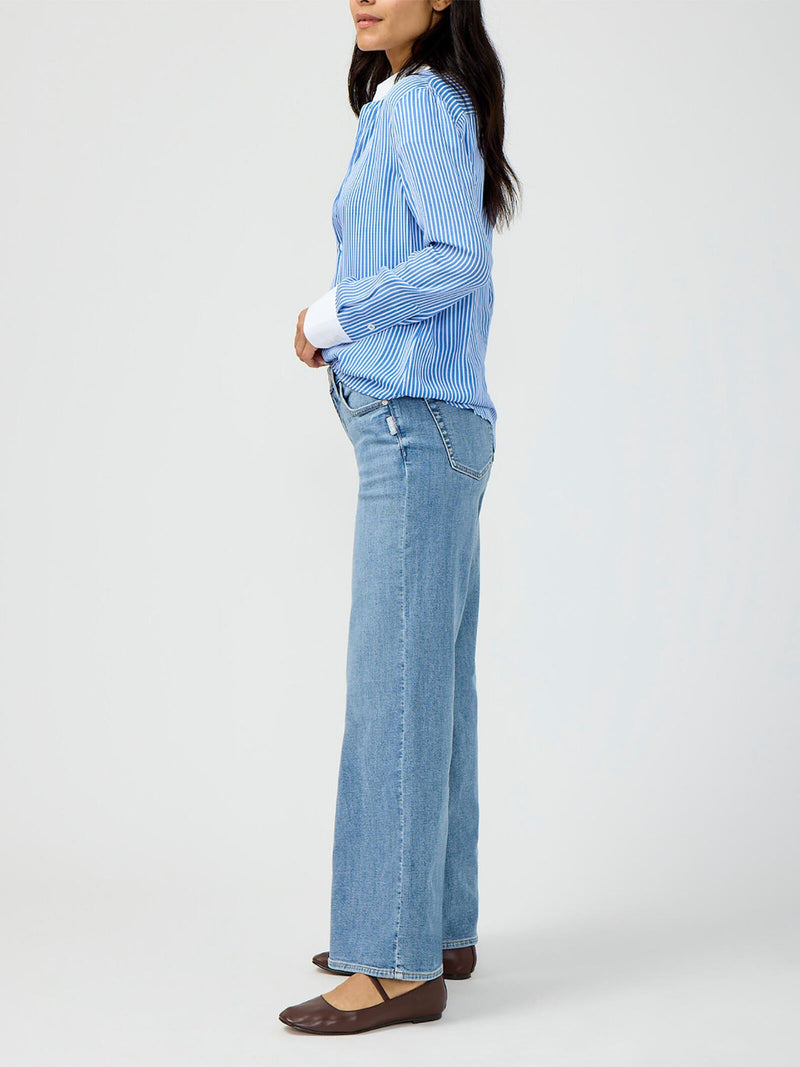 Woman wearing a blue striped shirt and light blue jeans on a white background