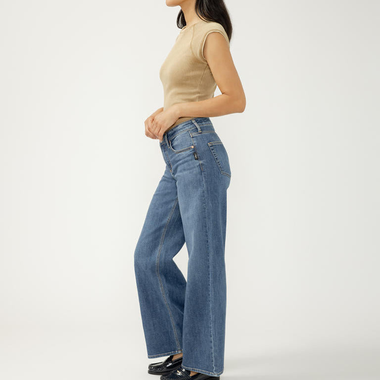 Woman wearing blue jeans and a beige top on a white background