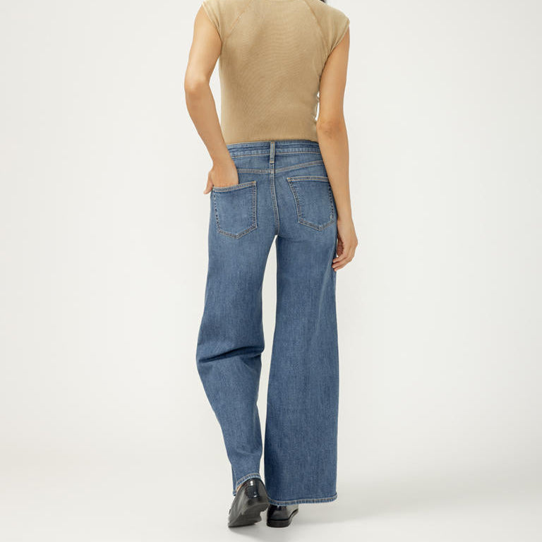 Person wearing a beige top and blue jeans on a white background