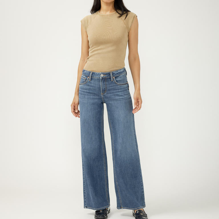 Person wearing a beige top and blue jeans on a white background